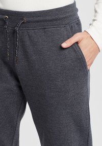 Mörkgrå sweatpants i mjukt material, med dragsko i midjan och metalldetaljer samt sidofickor. Slät textur, avslappnad design.