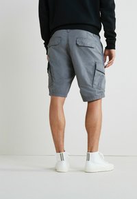 Szürke cargo shorts oldalsó zsebekkel, puha tapintású, térd hosszúságú, fehér, csíkos részletekkel ellátott magasszárú tornacipővel párosítva.