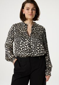 Black and cream patterned blouse with a collared neckline, button front, and long sleeves. Made of smooth fabric with a slightly loose fit.