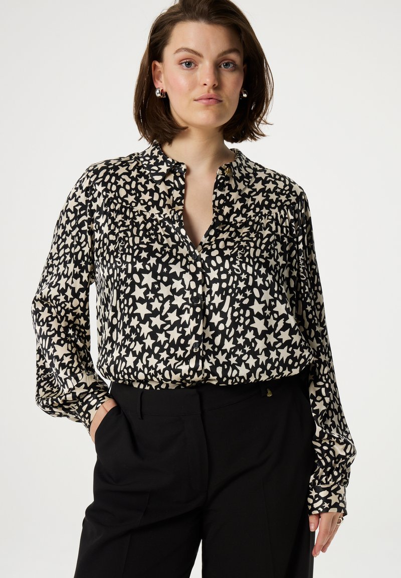 Black and cream patterned blouse with a collared neckline, button front, and long sleeves. Made of smooth fabric with a slightly loose fit.