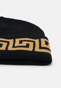 Black knit beanie with gold geometric pattern along the brim. Soft texture, cuffed design, and visible stitching detail.