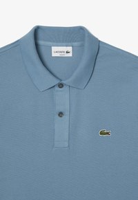 Polo azul de corte slim con tejido texturizado, dos botones oscuros y un pequeño logo bordado de cocodrilo verde.