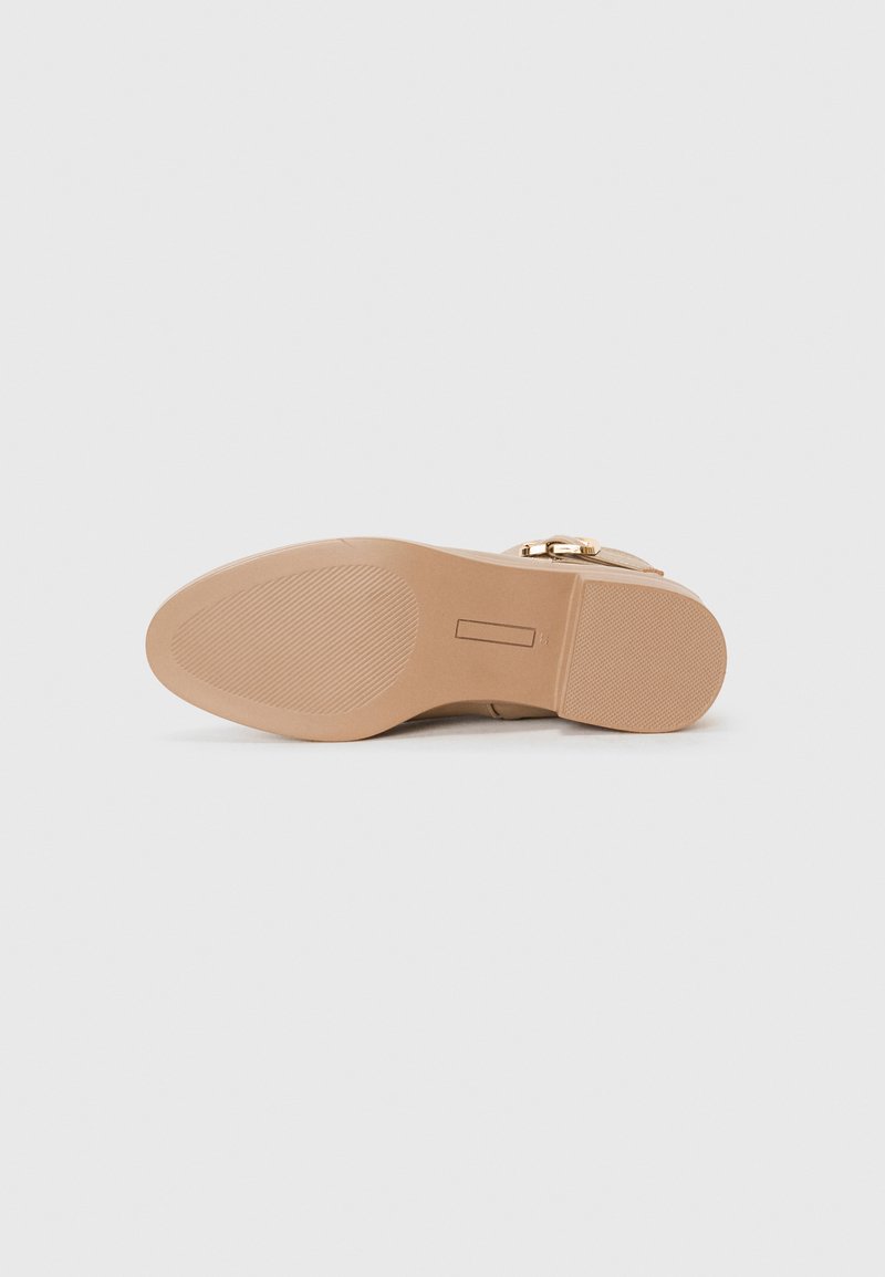 Suela de zapato de tacón alto beige con una textura suave, que cuenta con un detalle de hebilla dorada, forma curva y una superficie de agarre de goma con patrón.