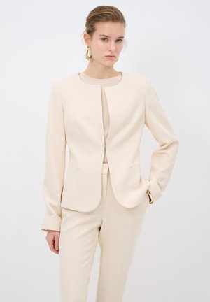 Beige přizpůsobený blazer s kulatým výstřihem, dlouhými rukávy a dvěma předními kapsami. Hladká struktura s přiléhavým siluetem, v kombinaci s odpovídajícími kalhotami.