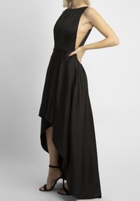 Schwarzes High-Low-Kleid mit ärmellosem Design, tailliertem Oberteil und seitlichen Ausschnitten. Glatte Textur mit einem schwingenden Rock und Riemchen-Pumps.