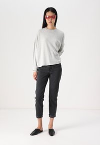 Top de mangas longas em cinza com franzidos, jeans curtos pretos, sapatos escorregadios pretos e óculos de sol com tonalidade rosa. Textura leve com punhos enrolados.