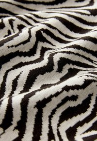 Textil s čierno-bielym zebrovým pruhovaním, s mäkkou, textúrovanou pleteninou, ktorá vytvára vlnitý vzhľad.