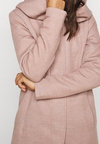 Cappotto rosa texture con cappuccio, dotato di chiusura con zip e maniche lunghe. Il tessuto presenta un motivo sottile ed è di vestibilità ampia.