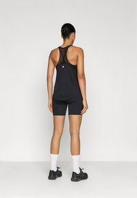 Μαύρο αθλητικό τοπ χωρίς μανίκια με πλέγμα στην πλάτη, σε συνδυασμό με μαύρο ποδηλατικό σορτς. Και τα δύο έχουν εφαρμοστή σχεδίαση, τονισμένη με στρογγυλεμένο τελείωμα και λεπτομέρεια με λογότυπο.