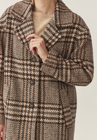 Wollen blend jas met een grote kraag, een beige, bruine en zwarte ruitpatroon, vier knopen en zijzakken. Getextureerde, oversized pasvorm.