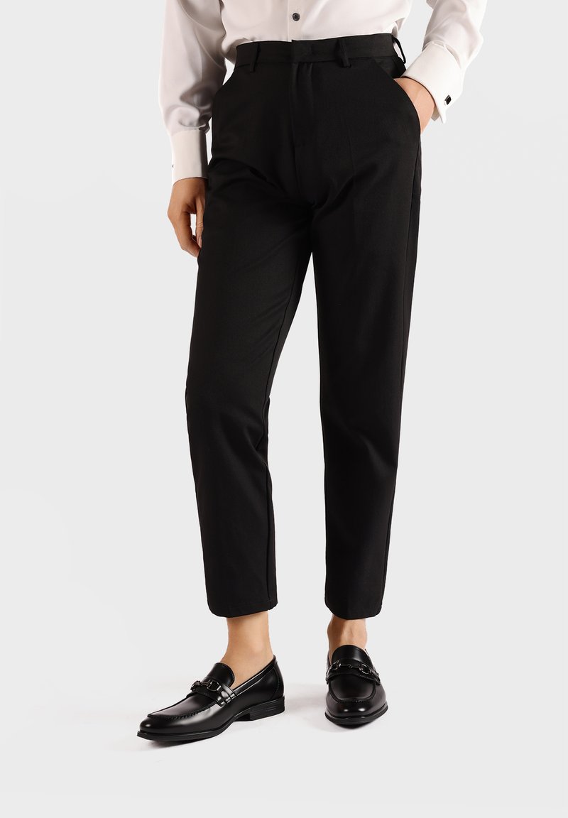 Pantaloni neri su misura con una vestibilità slim, caratterizzati da tasche laterali, una texture liscia e abbinati a mocassini neri lucidi.