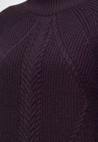 Pull tricoté violet foncé avec des motifs torsadés et un col montant côtelé.