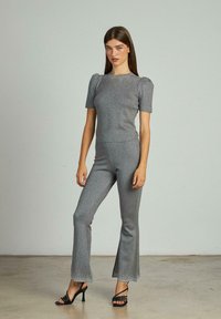 Grijze, glinsterende tweedelige set met korte mouwen en uitlopende broekspijpen. Gladde textuur. Open-teen zwarte bandjeshakken maken de look compleet.