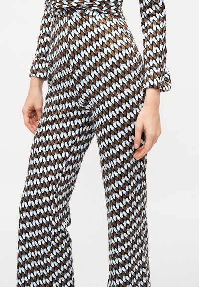 Γυναίκα που φοράει εφαρμοστή μακρυμάνικη μπλούζα και παντελόνι που ταιριάζουν, με καφέ, λευκό και μπλε οβάλ σχέδιο σε ανοιχτό φόντο.