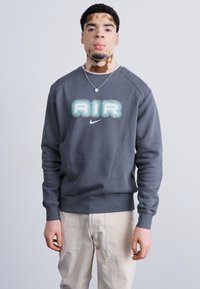 Gray sweatshirt with a rounded neckline, visible seams, and "AIR" graphic in light blue. Features a small Nike logo on the front.