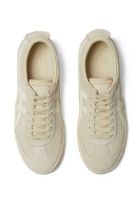 Beige Sneaker mit einem glatten Wildleder-Obermaterial, weißen Akzenten, Schnürverschluss und gummierter Sohle; verfügt über eine runde Zehenpartie und einen gepolsterten Kragen.