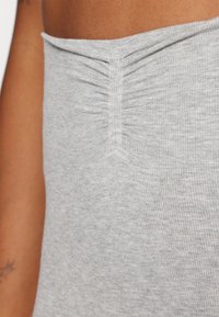 Κοντινό πλάνο κορμού που φοράει ανοιχτό γκρι ριμπ ύφασμα με λεπτομέρεια ραφής στο στήθος και εκτεθειμένους ώμο και χέρι.