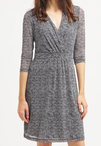 Svart och vit mönstrad klänning, halvgenomskinligt tyg, V-utsnitt, trekvartslånga ärmar, rynkad midja, knälång, avslappnad passform.