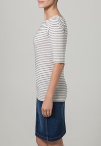 Weiß gestreites T-Shirt mit Dreiviertelärmeln, kombiniert mit einem dunkelblauen Jeansrock in Kniehöhe, der über eine vordere Naht und Taschen verfügt.