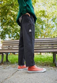 Svarta bomullbyxor med en avslappnad passform, med sidofickor och en liten vit logotyp. Pairade med orange högskoor.