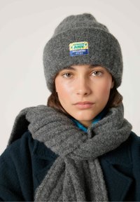 Grå uldbeanie med et farverigt patch og matchende ribbet tørklæde. Glat tekstur, rund form, og lagdelt stof synligt.