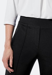 Schwarze taillierte Hose mit glatter Textur, ausgestattet mit vorderen Falten und seitlichen Taschen. Ein taillierter Bund ergänzt das elegante Design.