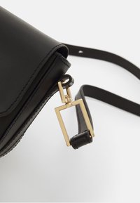 Borsa in pelle nera con una texture liscia, dotata di una chiusura rettangolare in hardware dorato e di una tracolla sottile. Cuciture distintive lungo i bordi.