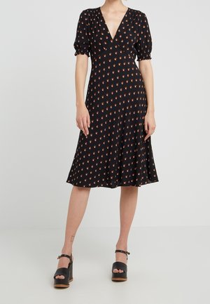 Femme portant une robe noire longueur genou avec un motif floral orange, des manches bouffantes, un décolleté en V et des sandales plateformes noires.