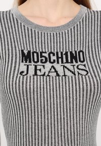 Šedý pruhovaný pletený svetr s kulatým výstřihem a výrazným černým logem "MOSCHINO JEANS" ve středu.
