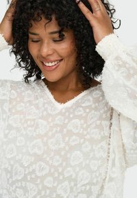 Bjela bluza s cvjetnim vezom, prozirna tkanina, v-izrez i naborane rukave s nabranim manžetama. Teksturirana površina dodaje detalj.