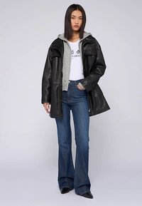 Chaqueta de cuero negra, sudadera con capucha gris, camiseta blanca con gráfico y vaqueros azules acampanados. Textura suave con capas casuales. Pantalones de corte ajustado.