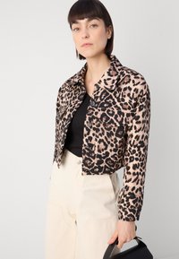Beskåret leopardmønstret jakke i beige og sort stoff, med krage, knappelukking og to frontlommer. Kombinert med svart topp og kremfargede bukser.