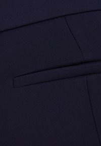 Granatowa tkanina o gładkiej fakturze z starannie ściegiem wszytą kieszenią szczelinową, zachowująca czysty, strukturalny wygląd.