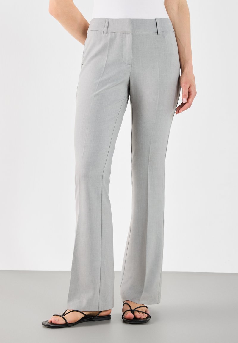 Pantalons gris évasés en tissu lisse, avec une taille plate et des poches latérales, associés à des sandales noires à lanières.