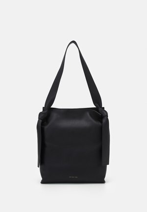 Czarna skórzana torba na ramię z szerokimi paskami związanymi na węzły po obu stronach oraz małym złotym logo „REJINA PYO” na środku na dole.