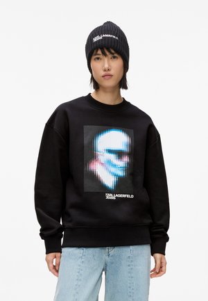 Sweatshirt en coton noir avec un graphique d'un visage stylisé dans des nuances de bleu et de rose ; comprend le texte "KARL LAGERFELD JEANS" en bas.
