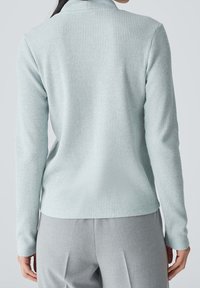 Ljust blå, ribbad långärmad topp med mockkrage och figurnära design, kombinerad med ljusgrå byxor som visar en slät yta.