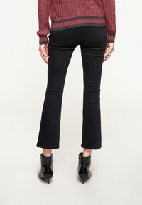 Jeans negros de campana con una textura suave, cintura media, y bolsillos traseros, combinados con botas negras hasta el tobillo con tacones curvados.