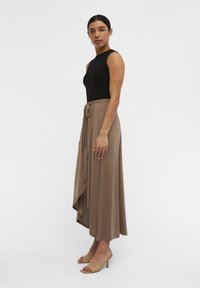 Sort ribbet tanktop parret med en strømlinet, beige maxiskirt med bindebånd i taljen og asymmetrisk kant, suppleret af beige hællet slippers.