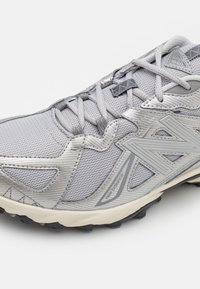 Zapatilla de running gris con parte superior de malla, superposiciones sintéticas y una suela de goma texturizada para una mejor tracción. Incluye un sistema de cordones tradicional.