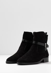Un paio di stivaletti neri in suede, con punta affusolata, tacco basso, cerniere laterali e cinturini decorativi alla caviglia con fibbie in argento.