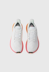 White athletic shoes with textured mesh upper, gray accents, and pink-orange gradient sole. Features traditional lacing and padded collar.