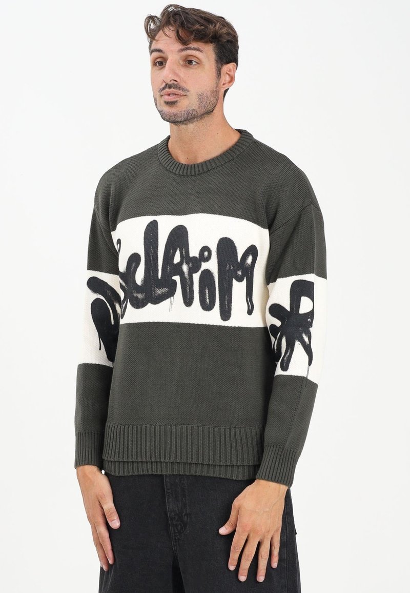 Maglione a maglia verde oliva con colletto a girocollo a coste, caratterizzato da audaci testi in stile graffiti neri e due righe orizzontali bianche.