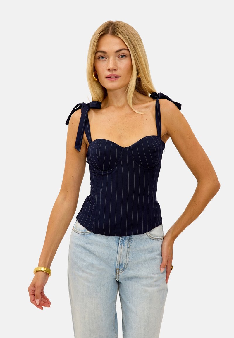 Bustier bleu marine à rayures avec des bretelles nouées. Conception ajustée et texture lisse, complétant un denim taille haute.
