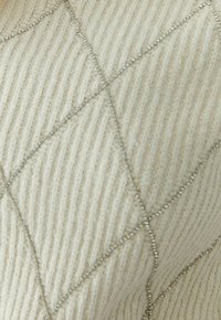 Crèmekleurige geribbelde tricotstof met een diamanten patroon omlijnd door dunne zilveren parels, wat een gestructureerd, fonkelend ontwerp creëert.