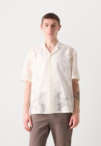 Cămașă scurtă cu mânecă închisă de culoare crem deschis, cu un model abstract subtil, cu închidere frontală cu butoane și guler. Materialul pare transparent și ușor.