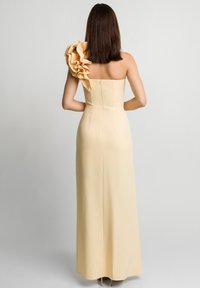 Żółta sukienka bez ramiączek z falbaniastym akcentem na jednym ramieniu, dopasowanym gorsetem i długą, zwiewną spódnicą. Gładki materiał z zapięciem na zamek błyskawiczny.