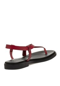 Sandalias de cuero rojo con suela plana y tiras finas, inclinadas para mostrar la parte posterior, destacando su diseño minimalista.