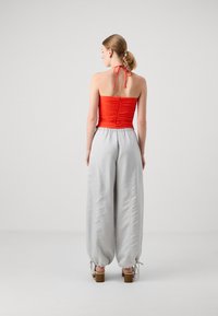 Rød rynket halterneck-top kombinert med lysegrå, brede bukser. Antrekket har et avslappet design med strikk i livet og åpen rygg.