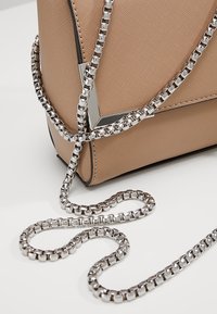 Borsa a tracolla in pelle marrone chiaro con finitura texturizzata e tracolla in catena argentata, dotata di un accento metallico geometrico sulla parte anteriore.